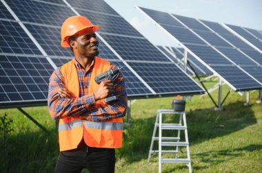 Güvenlik kaskı ve üniforma takan Afro-Amerikan elektrik mühendisinin portresi güneş panelleri kuruyor..