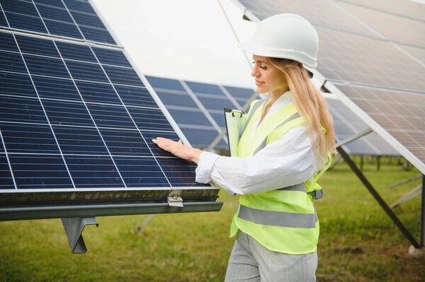Красивый молодой инженер с буфером обмена, стоящий возле солнечных панелей на открытом воздухе
.