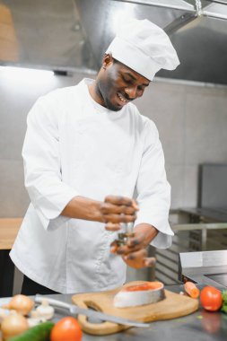 African American male chef preparing salmon fish in restaurant kitchen.