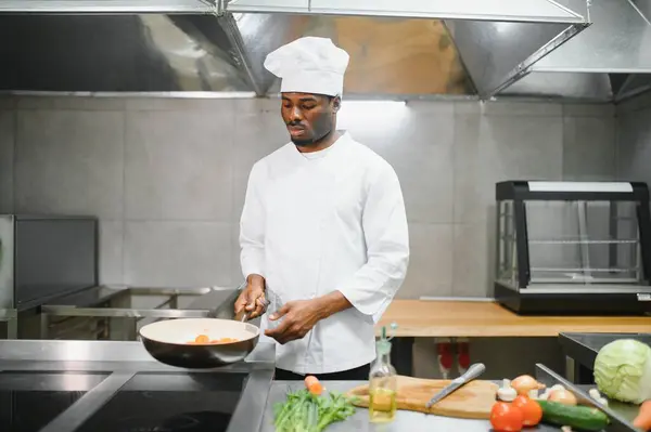 Stock image African American male chef frying vegetables in restaurant kitchen.