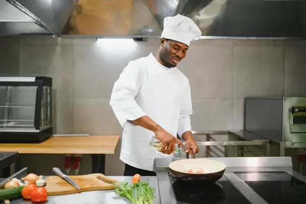 Stock image African American male chef frying vegetables in restaurant kitchen.