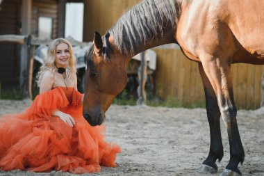 Güzel model kız uzun bir elbise içinde bir atla duruyor..