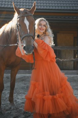 Güzel model kız uzun bir elbise içinde bir atla duruyor..