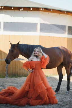 Güzel model kız uzun bir elbise içinde bir atla duruyor..