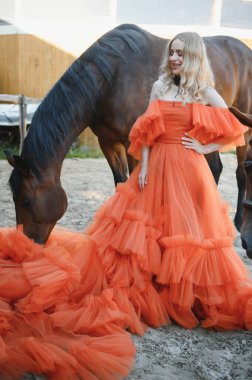 Güzel model kız uzun bir elbise içinde bir atla duruyor..