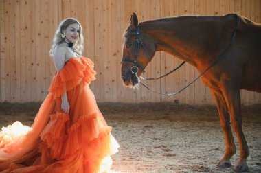 Güzel model kız uzun bir elbise içinde bir atla duruyor..