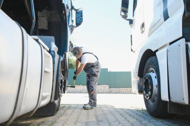 Yarı kamyon tekerleği bakım. Beyaz kamyonu makinist kamyon Servis Merkezi tekerlek göz alarak elinde büyük anahtar ile.