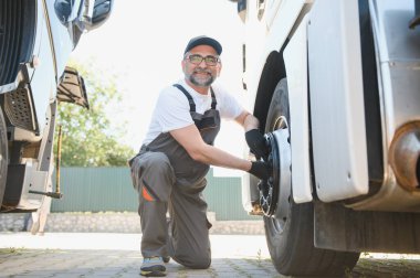 Yarı kamyon tekerleği bakım. Beyaz kamyonu makinist kamyon Servis Merkezi tekerlek göz alarak elinde büyük anahtar ile.