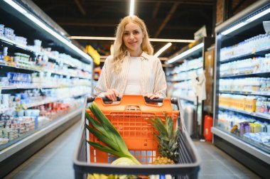 Markette ürünlere bakan genç bir kadın. Müşteriler marketten yiyecek alıyor..