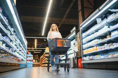 Markette ürünlere bakan genç bir kadın. Müşteriler marketten yiyecek alıyor..