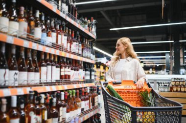 Hangi şarabı alacağına ve süpermarketten alışveriş yapacağına karar veren bir kadın..