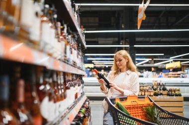 Hangi şarabı alacağına ve süpermarketten alışveriş yapacağına karar veren bir kadın..