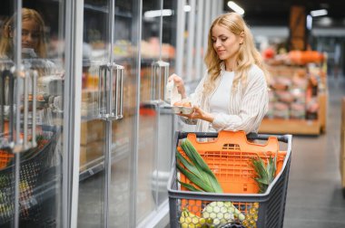 Young woman shopper in the grocery store choosing fresh chicken eggs.