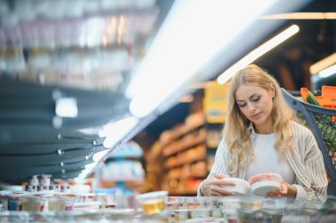 Genç havalı müşteri kadın süpermarket alışverişinde günlük kıyafet alışverişi yapıyor. Alışveriş arabasıyla alışveriş yapıyor. Hipermarketten ürünler seçiyor..