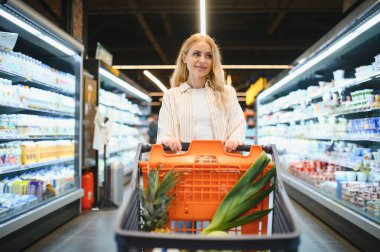 Markette ürünlere bakan genç bir kadın. Müşteriler marketten yiyecek alıyor..