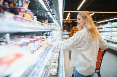Marketteki raflar arasında alışveriş arabalarını iten genç bir kadın..