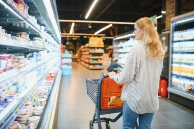 Markette ürünlere bakan genç bir kadın. Müşteriler marketten yiyecek alıyor..