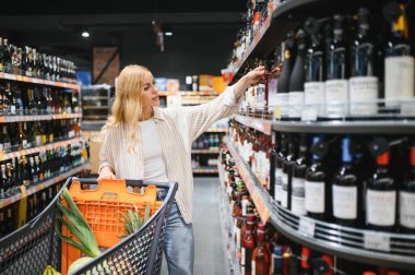 Hangi şarabı alacağına ve süpermarketten alışveriş yapacağına karar veren bir kadın..