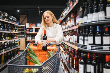 Kız süpermarkette şarap seçiyor. Kız süpermarkette şarap şişelerinin etiketlerini okuyor..