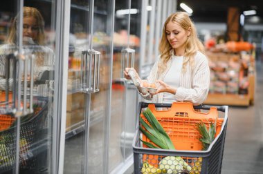 Marketteki raflar arasında alışveriş arabalarını iten genç bir kadın..