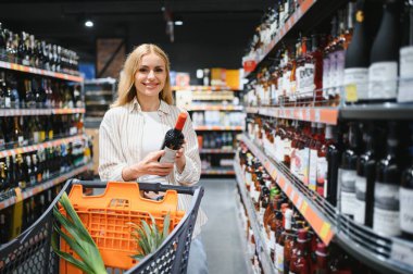 Hangi şarabı alacağına ve süpermarketten alışveriş yapacağına karar veren bir kadın..