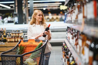 Hangi şarabı alacağına ve süpermarketten alışveriş yapacağına karar veren bir kadın..