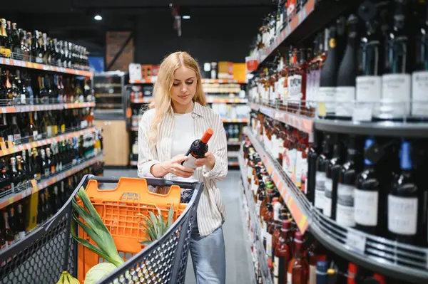 Hangi şarabı alacağına ve süpermarketten alışveriş yapacağına karar veren bir kadın..