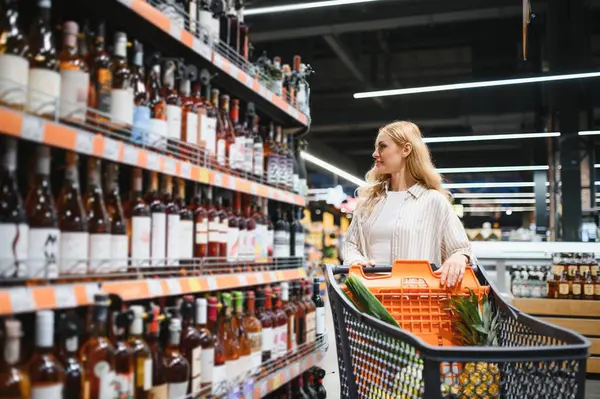 Hangi şarabı alacağına ve süpermarketten alışveriş yapacağına karar veren bir kadın..