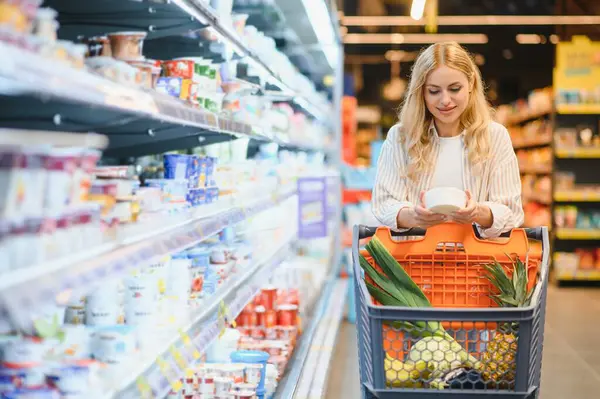 Genç havalı müşteri kadın süpermarket alışverişinde günlük kıyafet alışverişi yapıyor. Alışveriş arabasıyla alışveriş yapıyor. Hipermarketten ürünler seçiyor..