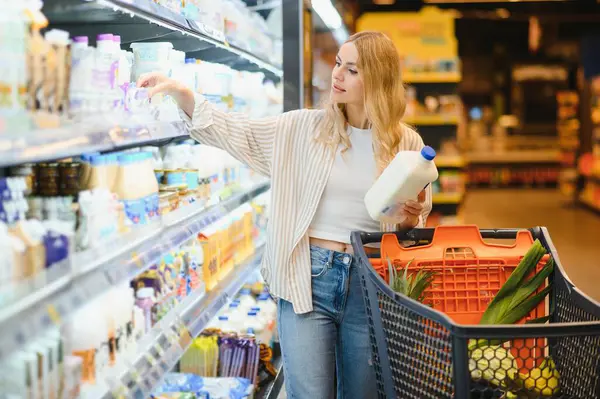 Marketteki raflar arasında alışveriş arabalarını iten genç bir kadın..