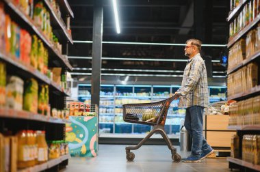 Marketten alışveriş yapan olgun bir adam. Arka plandaki diğer müşteriler. Tüketim kavramı.