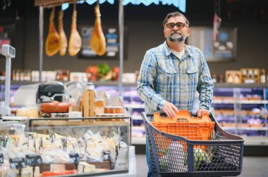 Markette alışveriş arabasını iten olgun bir adam market alışverişi, market alışverişi konsepti satın alıyor..