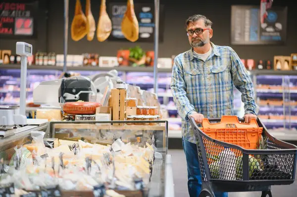 Marketten alışveriş yapan olgun bir adam. Arka plandaki diğer müşteriler. Tüketim kavramı.