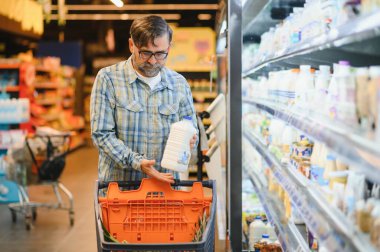 Süpermarkette elinde süt şişesi olan bir adam..