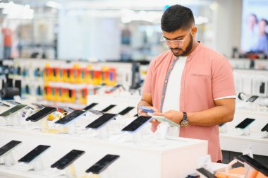 Elektronik mağazasındaki adam cep telefonunu seçiyor..
