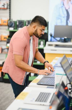 Erkek bir alıcı elektronik mağazasının bilgisayar bölümündeki dizüstü bilgisayarlara bakar. Alıcı modern bir teknoloji mağazasında dizüstü bilgisayar seçiyor.