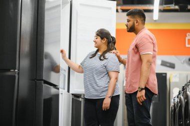 Genç Hintli çift, memnun müşteriler eşyalar dükkanında buzdolabı seçiyor..