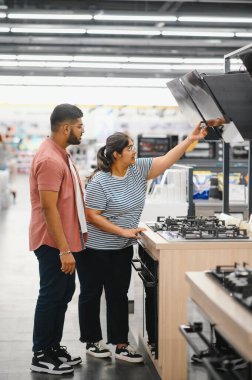 Couple of young customers looking at buildin cookers in domestic appliances shop. clipart