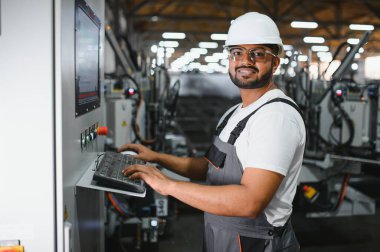 Gülümseyen ve mutlu çalışan. Fabrikada sanayi işçisi. Turuncu şapkalı genç teknisyen..