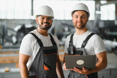 Fabrika işçisi ve mühendisi metal levha endüstriyel şantiyesinde birlikte çalışıyorlar, bilgisayardaki makine işlemini kontrol ediyorlar ve güvenlik için başlık takıyorlar.