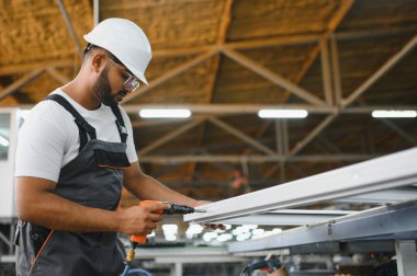 Özel üniformalı mutlu Hintli erkek fabrika işçisi ve metal pencere ve kapılarda alüminyum çerçeve tutan beyaz başlıklı adam..