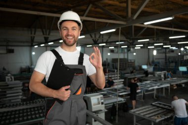 Gülümseyen ve mutlu çalışan. Fabrikadaki endüstriyel işçilerin portresi. Beyaz şapkalı genç teknisyen..