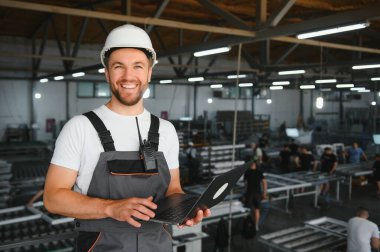 Genç bir erkek mühendis plastik pencere çerçevelerinin üretimini denetliyor.