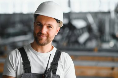 Endüstriyel erkek mühendis, arkasında ağır bir fabrikada dururken beyaz kask takıyor. Endüstriyel makinelerde çalışmanın ve fabrikadaki güvenlik sistemini kontrol etmenin bakımı.