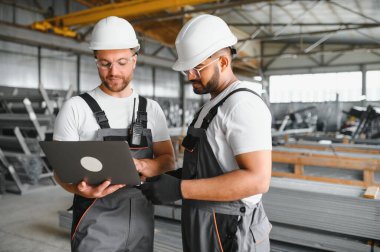 Hard Hats 'ta İki Ağır Sanayi Çalışanı Fabrika' da İş Bulma Görevlerini Tartışıyor, Laptop Bilgisayarını Kullanıyor.