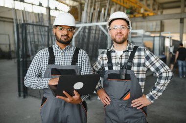 Güvenlik üniforması ve beyaz kaskla birlikte çalışan iki mühendis fabrikada çalışıyor..