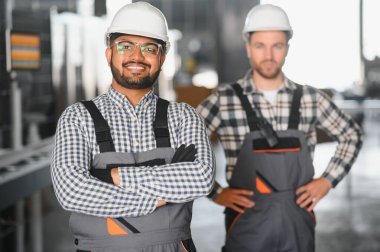 Güvenlik üniforması ve beyaz kaskla birlikte çalışan iki mühendis fabrikada çalışıyor..