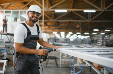 Özel üniformalı mutlu Hintli erkek fabrika işçisi ve metal pencere ve kapılarda alüminyum çerçeve tutan beyaz başlıklı adam..