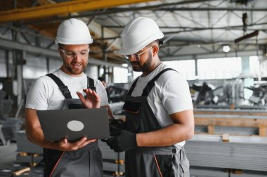 Hard Hats 'ta İki Ağır Sanayi Çalışanı Fabrika' da İş Bulma Görevlerini Tartışıyor, Laptop Bilgisayarını Kullanıyor.