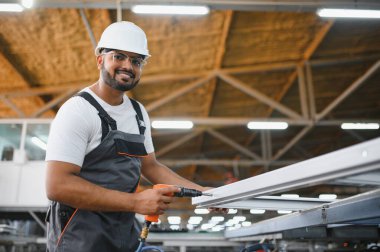 Gülümseyen ve mutlu çalışan. Fabrikada sanayi işçisi. Turuncu şapkalı genç teknisyen..